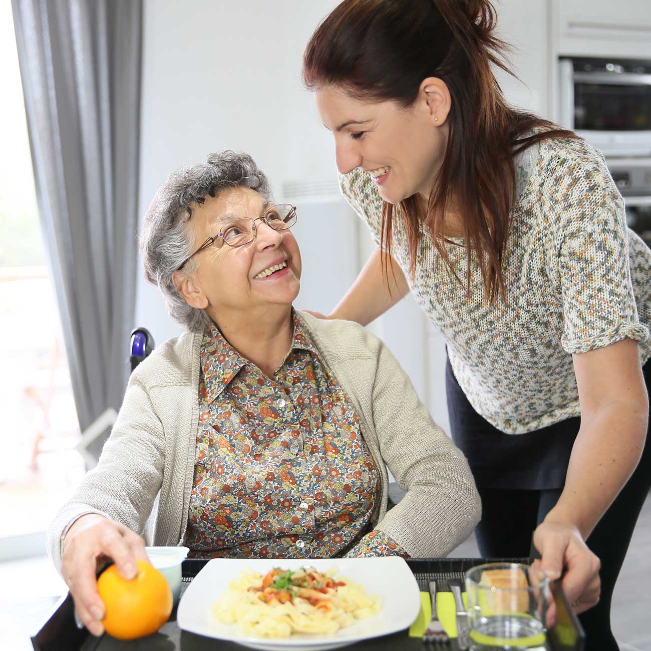 A trained companion caregiver serves a meal to a senior home care client who is in a wheelchair.